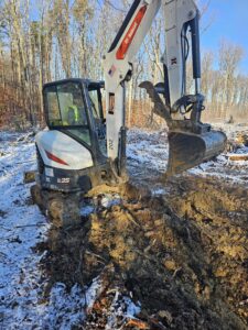 White Bobcat excavator digging in the woods.