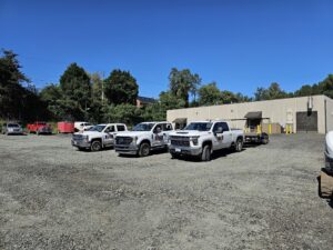 Four white trucks parked in gravel lot.