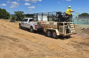 Truck and trailer spraying green grass seed.