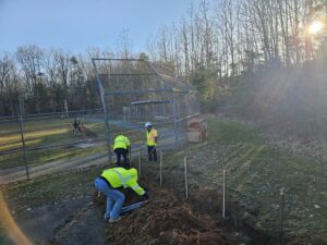 Workers digging a trench near a baseball field.